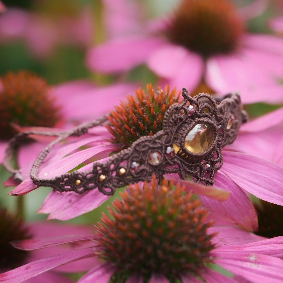 Bracelet elfique fait main en coton brun, décoré d’une citrine naturelle ovale et de perles facettées en grenat. Bijou lumineux et unique de la collection Clairière de Miel, photographié en gros plan pour révéler la beauté des pierres naturelles.
