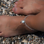 Duo de Bracelets de cheville bohème, ambiance plage et été sur les îles. Bijoux de pieds assortis. Micro macramé en fil de coton couleur lin beige avec une pierre de larimar bleu ciel accompagné d'une perle goutte argenté. Système de réglage à coulisse à l'arrière. Bijou porté sur une cheville dénudée à la peau caramel dans un univers sirène, marin avec plage de  coquillages
