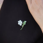 Mini broche fleur blanche en micro macramé avec cœur en labradorite bleu-vert, épinglée sur manteau en laine marron foncé, bijou elfique et bohème fait main.