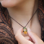 Collier elfique réglable en micro macramé avec citrine ovale jaune pâle et fleur orange dorée. Bijou floral et lumineux de la collection Clairière de Miel, porté par une femme à la peau claire et cheveux bruns.