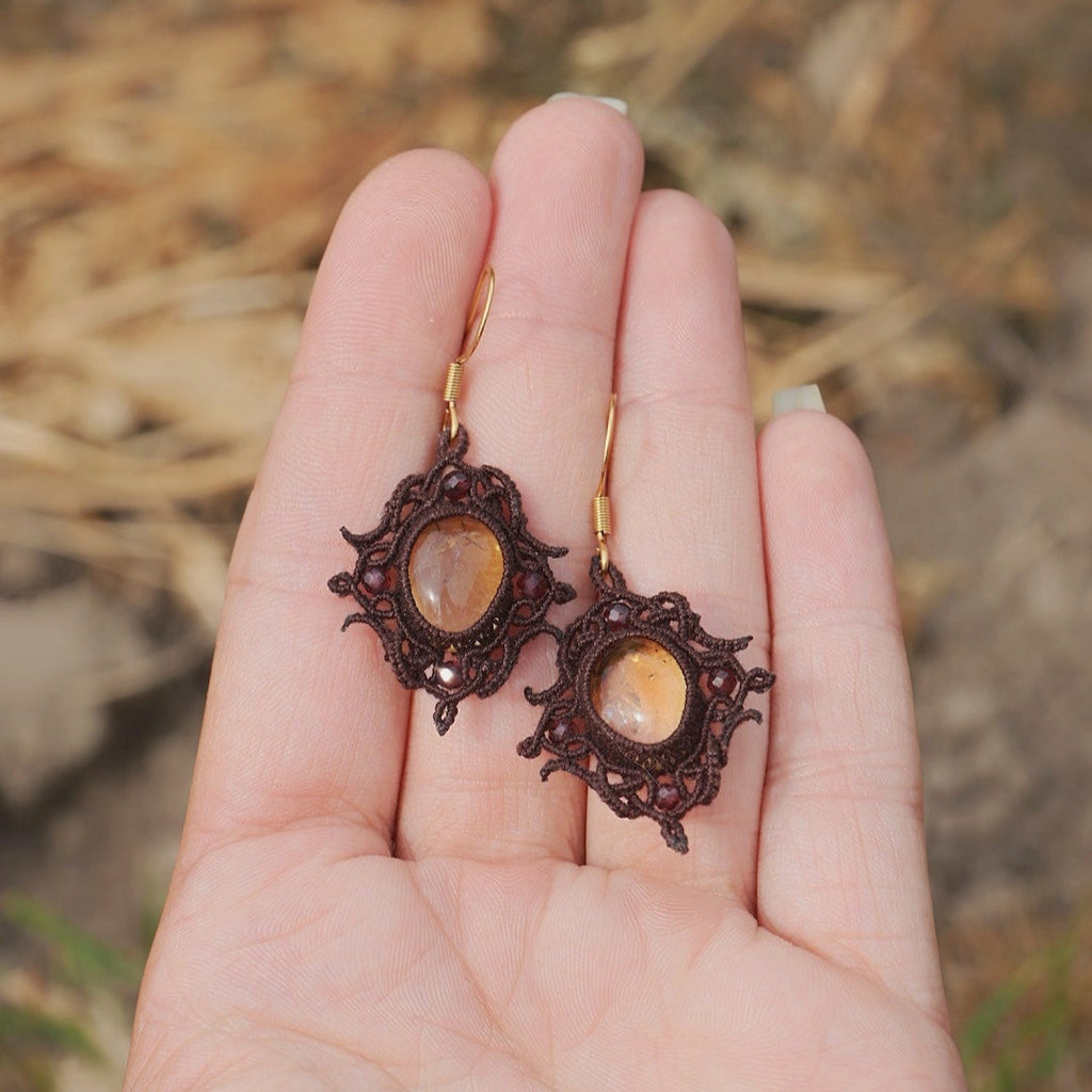 « Boucles d’oreilles artisanales elfique en citrine et grenat, bijou bohème léger et raffiné tissé en micro macramé, présenté dans une main à peau claire »