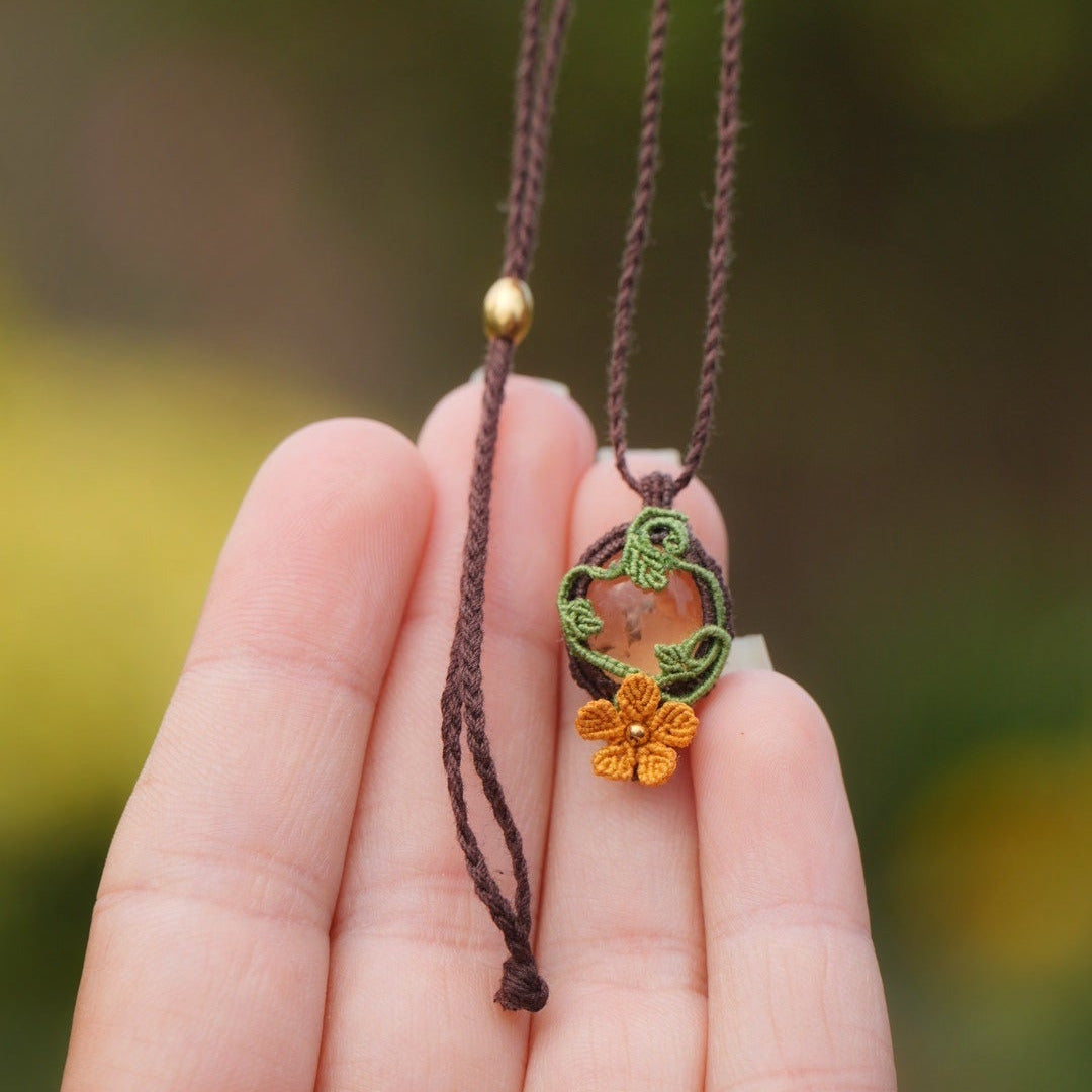 Collier artisanal elfique en macramé avec citrine naturelle et fleur orange, collection Clairière de Miel. Présenté dans une main féminine à la peau claire, pour mettre en valeur les détails et la finesse du tissage fait main.