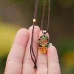 Collier artisanal elfique en macramé avec citrine naturelle et fleur orange, collection Clairière de Miel. Présenté dans une main féminine à la peau claire, pour mettre en valeur les détails et la finesse du tissage fait main.