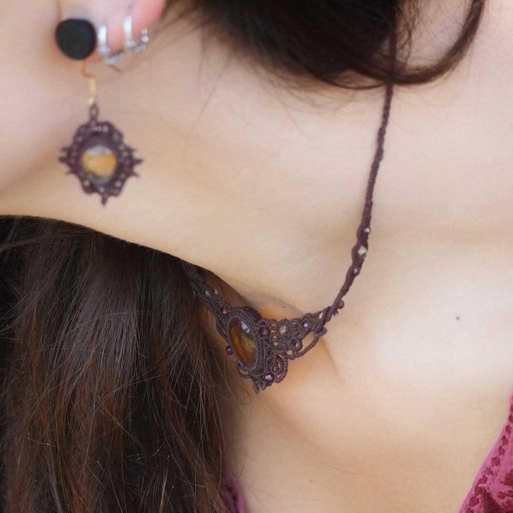 Collier ras de cou elfique en micro macramé brun, orné de citrine jaune dorée et de grenat rouge rosé. Bijou bohème réglable, porté par une femme à la peau claire et cheveux bruns, assorti à un vêtement rose profond.