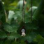 Bijou pendentif en labradorite blanche suspendu verticalement au milieu de de feuilles d'ancolie mouillées par la pluie, collier elfique bohème réglable. Coton et Astrance