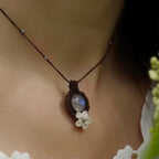 Collier elfique en labradorite blanche porté par un modèle à peau claire et cheveux bruns, vêtue d’habits féériques en dentelle blanche, bijou bohème artisanal réglable. Coton et Astrance
