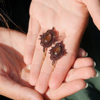 « Boucles d’oreilles artisanales elfique en citrine et grenat, bijou bohème léger et raffiné tissé en micro macramé, présenté dans une main à peau claire »