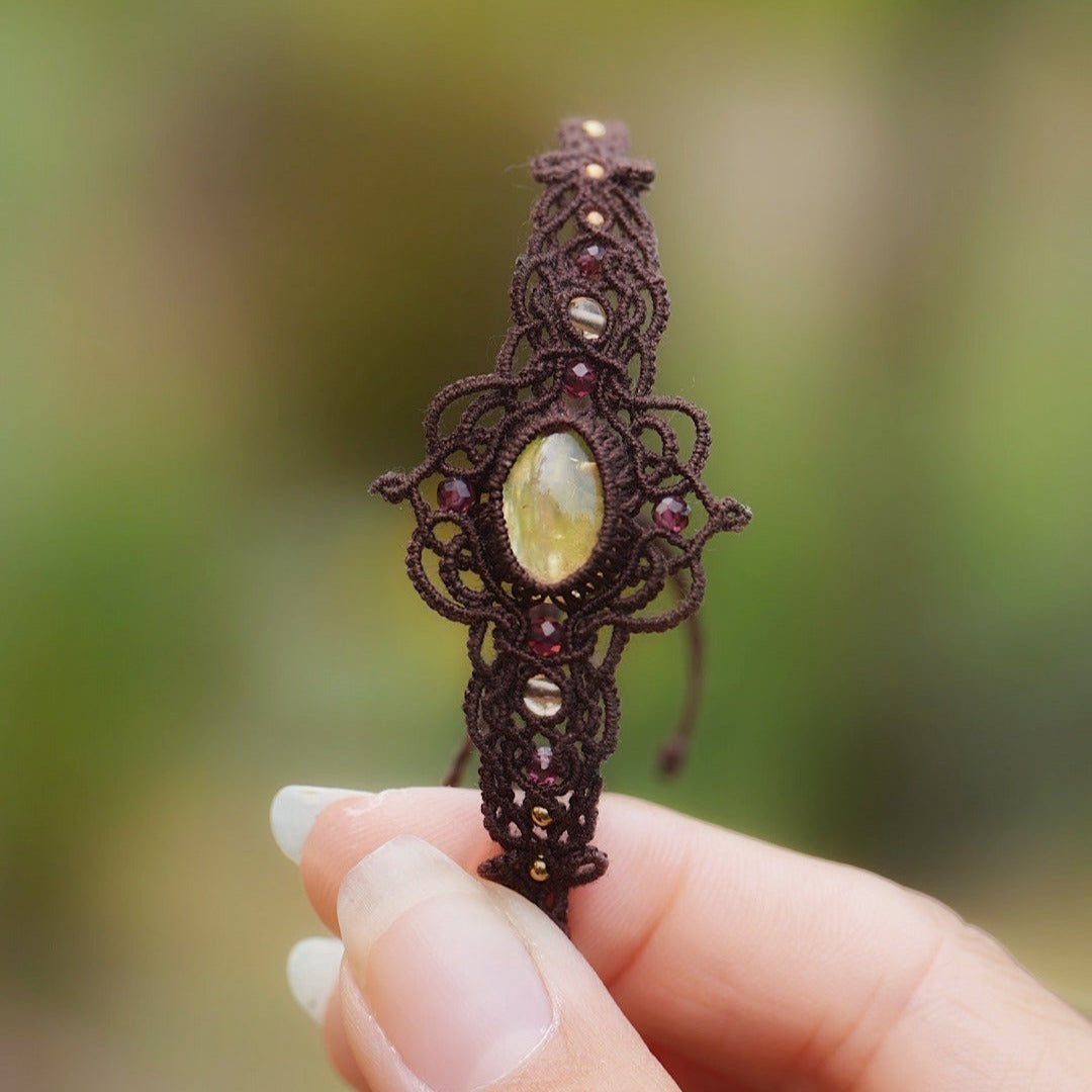 Bracelet elfique fait main en coton brun, décoré d’une citrine naturelle ovale et de perles facettées en grenat. Bijou lumineux et unique de la collection Clairière de Miel, photographié en gros plan pour révéler la beauté des pierres naturelles.
