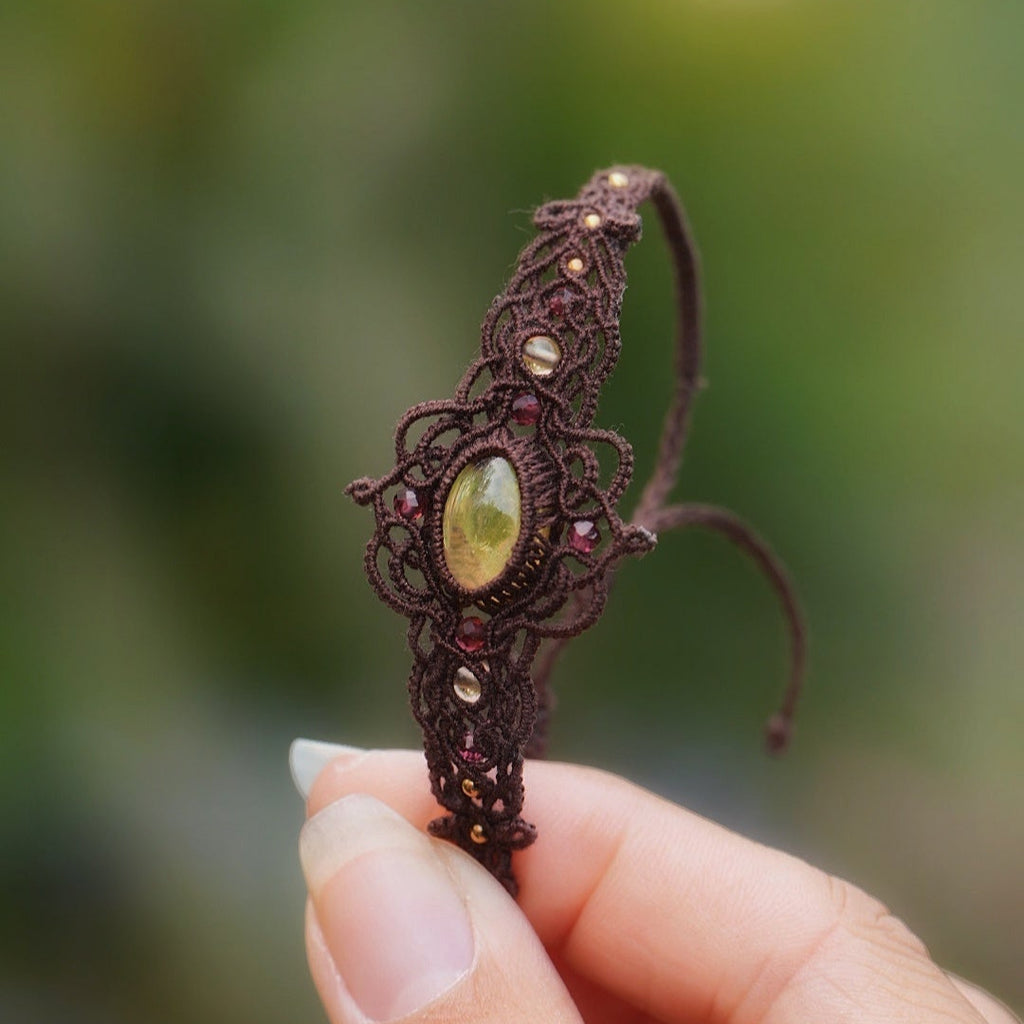 Bracelet elfique fait main en coton brun, décoré d’une citrine naturelle ovale et de perles facettées en grenat. Bijou lumineux et unique de la collection Clairière de Miel, photographié en gros plan pour révéler la beauté des pierres naturelles.