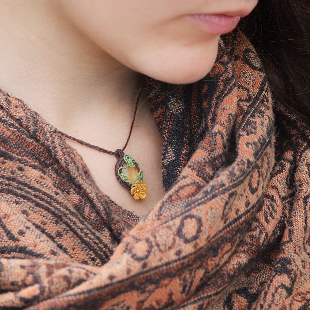 Collier elfique réglable en micro macramé avec citrine ovale jaune pâle et fleur orange dorée. Bijou floral et lumineux de la collection Clairière de Miel, porté par une femme à la peau claire et cheveux bruns.