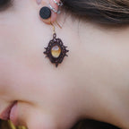 « Boucles d’oreilles elfiques losange en citrine dorée et grenat rouge, portées sur modèle à peau claire et cheveux bruns – Bijoux bohèmes artisanaux en micro macramé fait main en France »