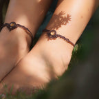 Bijoux de pieds, paire assortie de bracelets de chevilles à ambiance bohème celtique elfique. Fil marron foncé fin tissé en micro macramé avec entrelacs et arabesques, pierre centrale ovale petite taille jaune miel translucide. Bijoux hippie, bohème avec inspiration nature. Chevillères portées sur des chevilles à la peau pâle, bijoux de face avec jeu d'ombre et lumière et fleurs jaune en haut à droite.