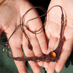 Bijou elfique artisanal réglable en citrine jaune et grenat rouge, tissé en macramé brun. Collier ras de cou bohème, présenté dans une main féminine à la peau claire, mettant en valeur la finesse du tissage.