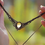 Collier elfique en macramé fait main, avec citrine ovale translucide jaune ambré et perles de grenat rouge rosé. Bijou artisanal de la collection Clairière de Miel, présenté en main pour révéler la transparence lumineuse de la pierre.