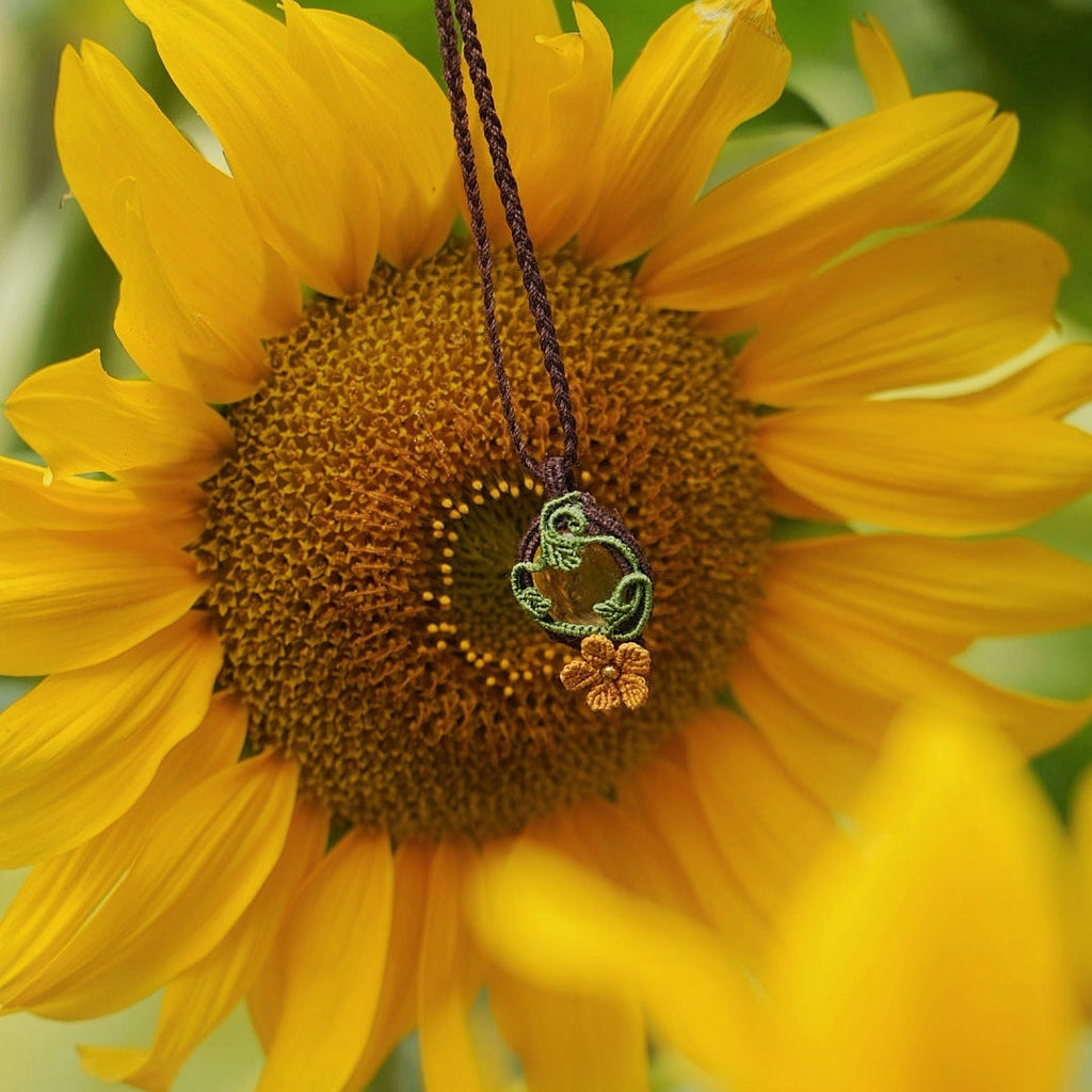 Collier elfique floral en citrine et macramé, fait main en France. Pièce artisanale réglable de la collection Clairière de Miel, photographiée au cœur de la nature au centre d'une fleur de tournesol pour souligner son inspiration bohème et féérique.