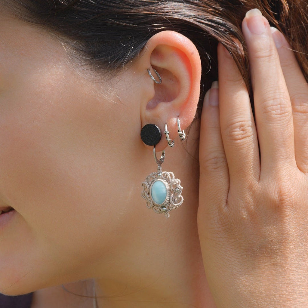 Parure Trésors d'Ecume composée d'une paire de boucles d'oreilles pendentes avec collier ras de cou assorti. Larimar bleu ciel ovales pour les boucles et en poire pointe en bas pour le collier. 3 Perles en nacre blanche pour le collier. Perles acier inoxydable argenté pour les deux pour le côté luxe et précieux. Dormeuses en acier inoxydable pour un port assuré. Fil de Coton couleur lin naturel (beige gris) de 0, 5 mm tissé en micro-macramé en relief version celtique. Bijoux porté femme brune peau caramel 