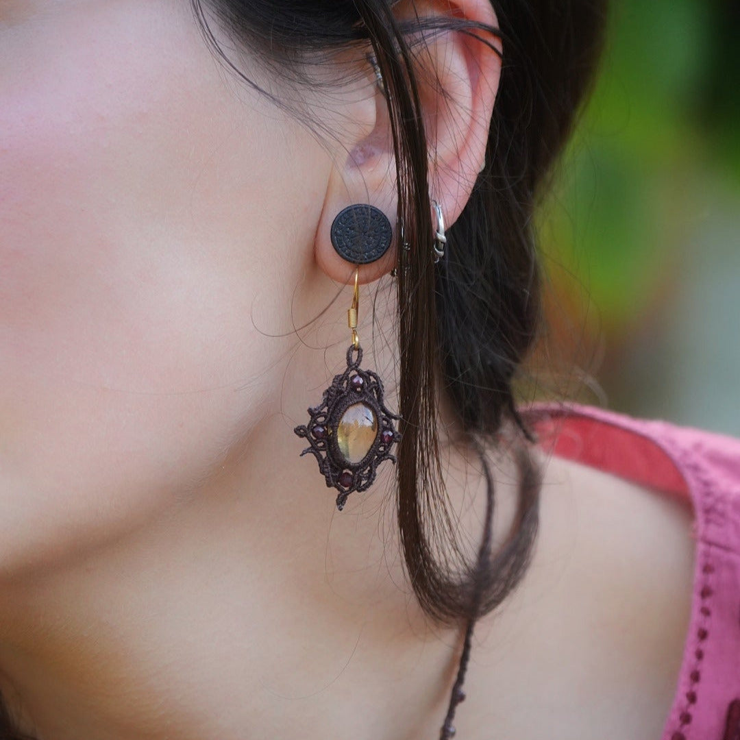 « Boucles d’oreilles elfiques losange en citrine dorée et grenat rouge, portées sur modèle à peau claire et cheveux bruns – Bijoux bohèmes artisanaux en micro macramé fait main en France »