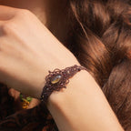 Bracelet large elfique en micro macramé brun, orné d’une citrine jaune pâle et de perles de grenat rouge rosé. Bijou bohème et artisanal réglable, porté au poignet d’une femme à la peau claire.