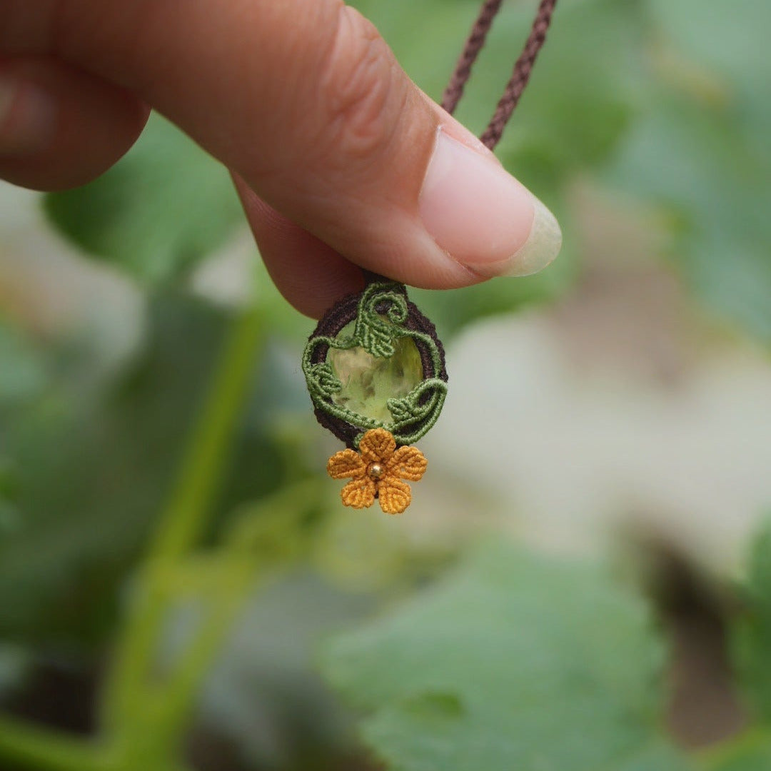 Collier elfique floral en citrine et macramé, fait main en France. Pièce artisanale réglable de la collection Clairière de Miel, photographiée au cœur de la nature parmi des feuilles de courge pour souligner son inspiration bohème et féérique.