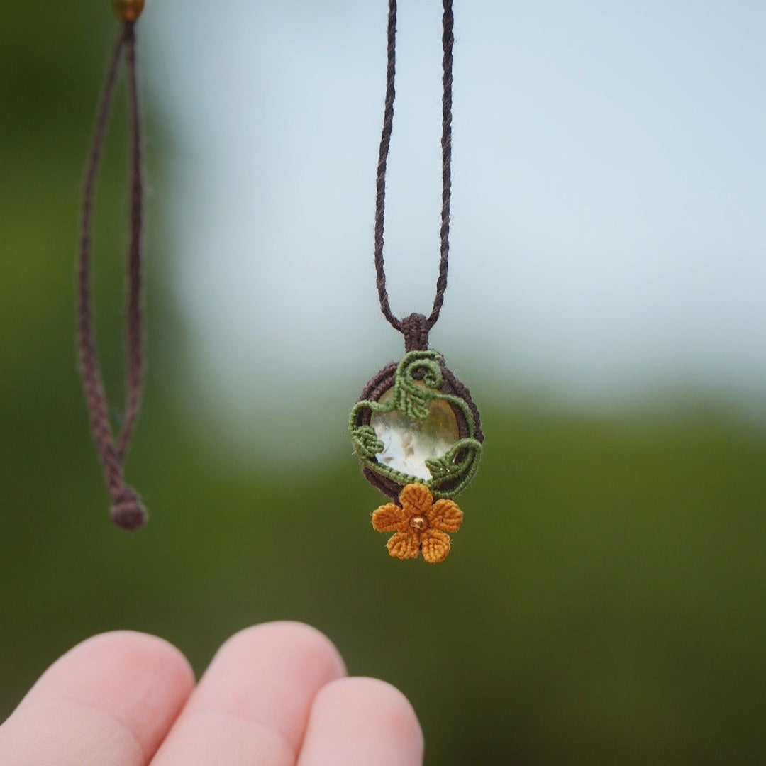 Collier en micro macramé artisanal avec citrine naturelle translucide jaune pâle et fleur orange en relief. Bijou elfique et bohème, collection Clairière de Miel, présenté dans une main pour révéler la transparence lumineuse de la pierre.