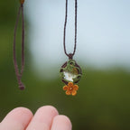 Collier en micro macramé artisanal avec citrine naturelle translucide jaune pâle et fleur orange en relief. Bijou elfique et bohème, collection Clairière de Miel, présenté dans une main pour révéler la transparence lumineuse de la pierre.