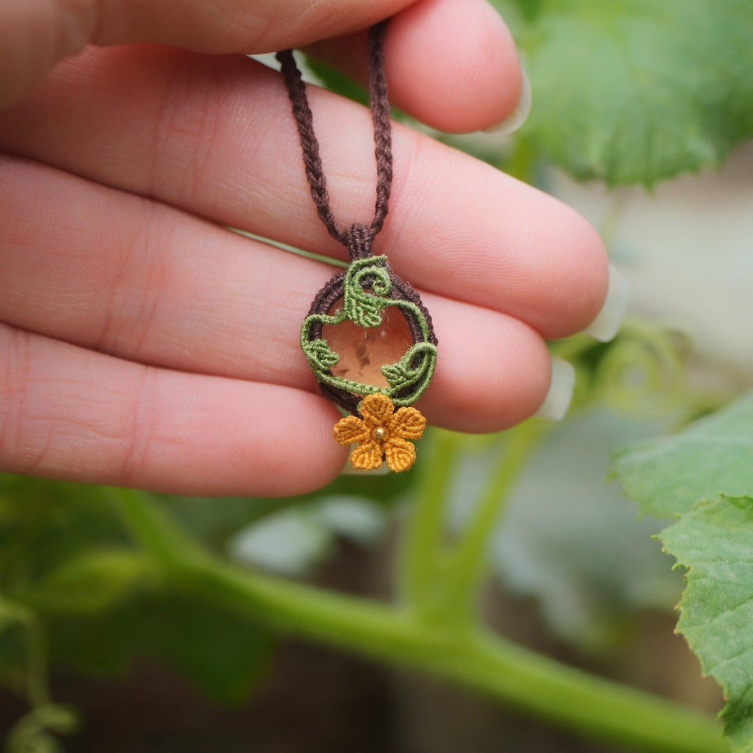 Collier elfique floral en citrine et macramé, fait main en France. Pièce artisanale réglable de la collection Clairière de Miel, photographiée au cœur de la nature parmi des feuilles de courge pour souligner son inspiration bohème et féérique.